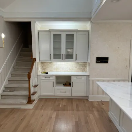 Bright kitchen area with white cabinetry, subway tile backsplash, wooden stairs, and light hardwood flooring.