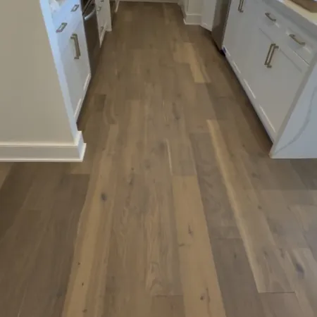 Modern kitchen with white cabinets, stainless steel appliances, and light wood flooring in a narrow layout.