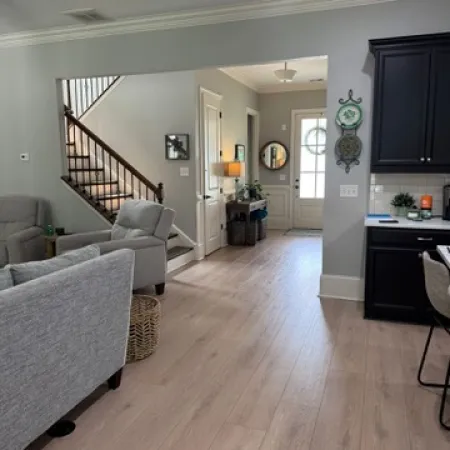 Modern open living space with light wood floors, gray walls, staircase, and dark kitchen cabinets.
