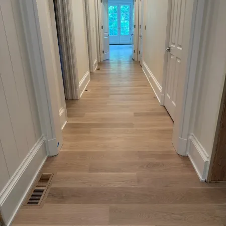 Bright hallway with light wood flooring, white walls, multiple doors, and a glass door at the end.