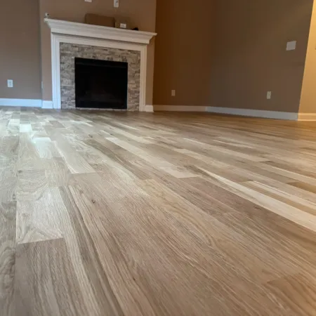 Close-up of light wood laminate flooring with a white fireplace and beige walls in an empty room.