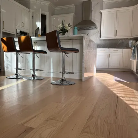 Modern kitchen with white cabinets, stainless steel appliances, wooden bar stools, and natural light on hardwood floor.
