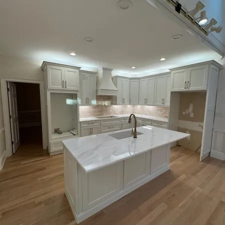 Modern white kitchen with marble island, brushed nickel faucet, subway tile backsplash, and hardwood floors.
