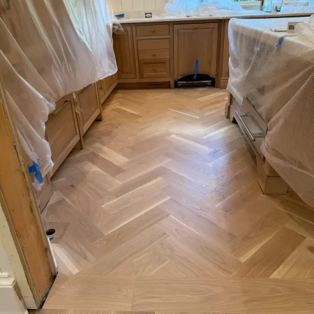 Newly installed herringbone hardwood floor in a kitchen under renovation with covered cabinets and island.