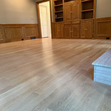 Empty room with light wood flooring, built-in wooden cabinets, beige walls, and white door in the background.