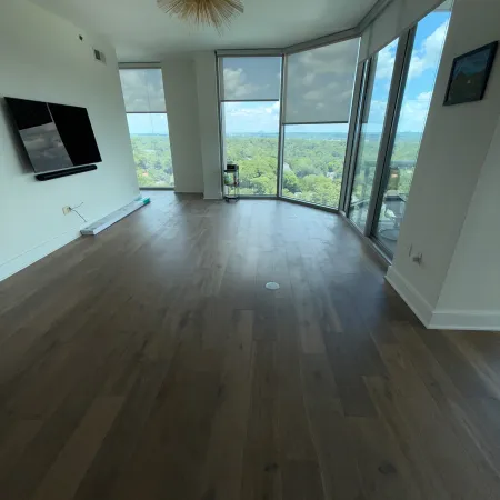 Empty modern living room with wood flooring, large windows, and a panoramic green landscape view outside.