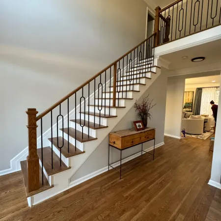 Modern wooden staircase with black metal railings beside a wooden console table on hardwood flooring in a spacious hallway.