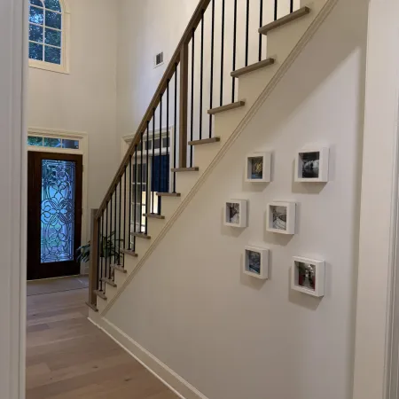 Modern staircase with wood steps and black railings, decorated wall art, chandelier, and stained glass front door.