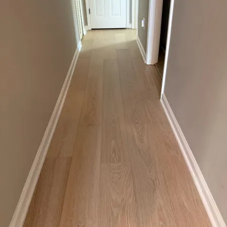 Narrow hallway with light-colored wood flooring, beige walls, and white door at the end.