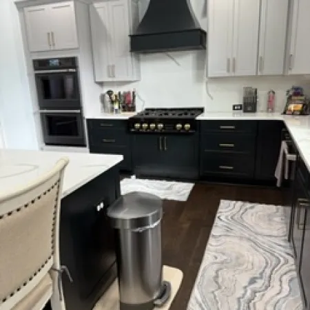 Modern kitchen with black and white cabinetry, stainless steel appliances, and a patterned area rug on dark hardwood floors