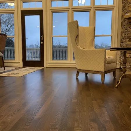 Cozy living room with large windows, dark wooden floor, beige armchair, stone fireplace, and outdoor balcony view.