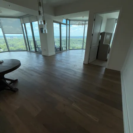 Spacious modern apartment with dark wood flooring and large windows offering panoramic forest and city views.