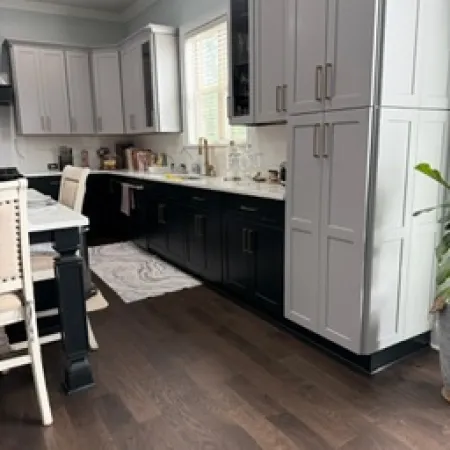 Modern kitchen with two-tone cabinetry, dark hardwood floors, white countertops, and a window above the sink.