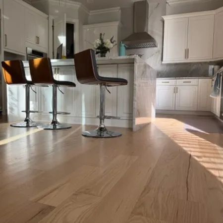 Bright modern kitchen with white cabinets, stainless steel appliances, and wooden bar stools on light hardwood floor.
