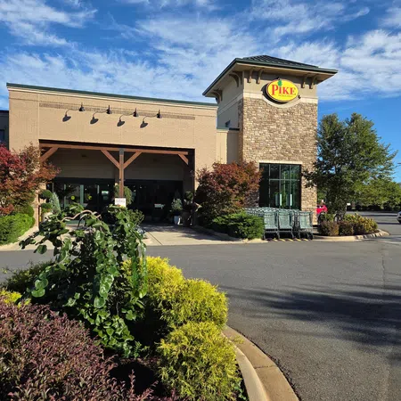 Pike Nurseries store front with landscaped bushes, shopping carts, and a blue sky with scattered clouds.