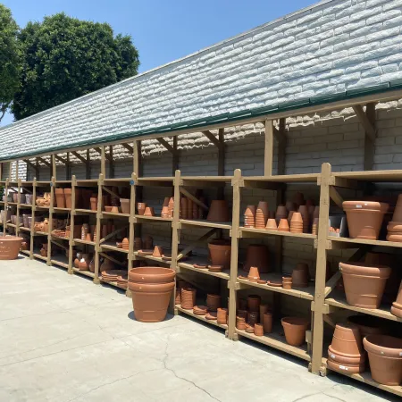 Outdoor display of various terracotta pots and planters neatly arranged on wooden shelves under a shaded structure.