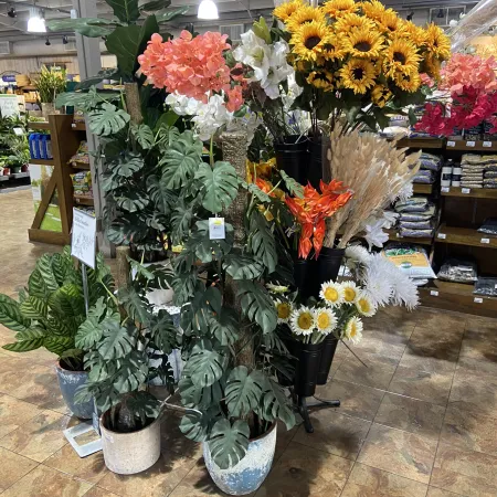 Indoor garden center display with potted plants and vibrant artificial flowers including sunflowers and hydrangeas.