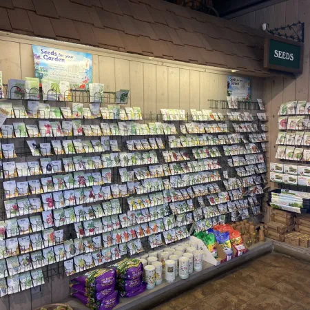 Wall display of various seed packets and gardening supplies in a store with wooden walls and signage.