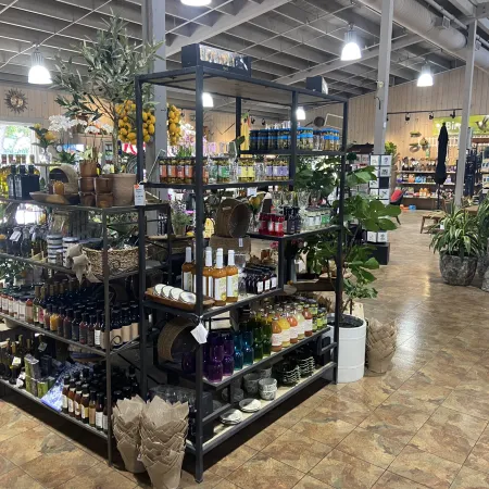 Interior of a store with metal shelves displaying bottles, jars, plants, and pottery under bright ceiling lights.