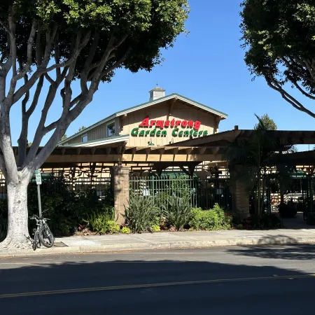 Entrance of Armstrong Garden Centers with wooden pergola, trees, and parked bike on a sunny day.