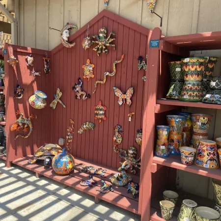 Colorful ceramic art pieces including animals and pots displayed on red wooden shelves and board outdoors.