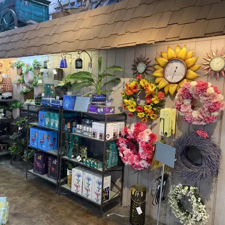 Shop display with floral wreaths, decorative clocks, potted plants, and various home decor items on shelves.