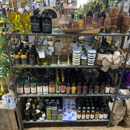 Store display shelf with various gourmet oils, sauces, spices, and wooden bowls arranged in a rustic market setting