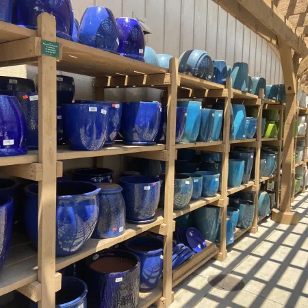 Shelves filled with blue and turquoise ceramic pots displayed under wooden pergola casting patterned shadows.