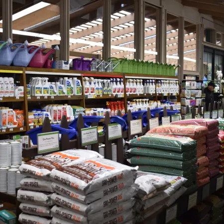 Indoor garden center aisle with bags of soil, colorful watering cans, and shelves of gardening products under wooden beams