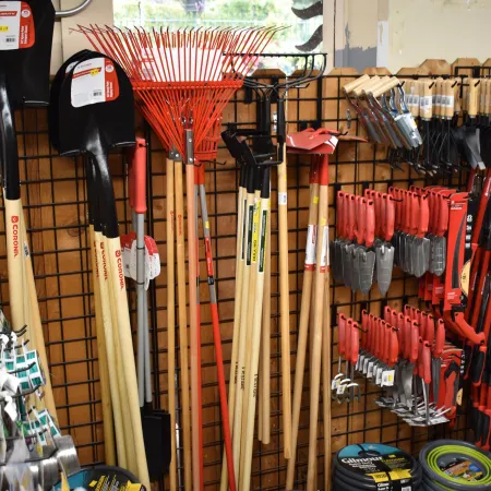Display of various garden tools including shovels, rakes, hoes, and hand tools on a store wall.