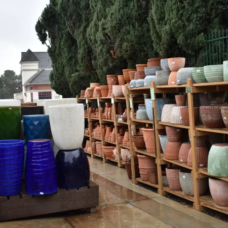 Outdoor display of various colorful ceramic pots and planters arranged on wooden shelves on a rainy day.