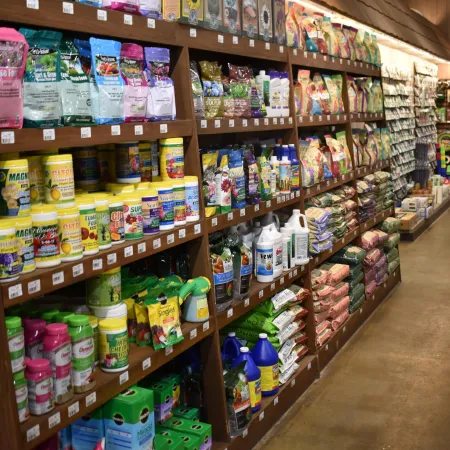 Aisle in garden store with shelves stocked with plant fertilizers, seeds, soil bags, and gardening supplies.