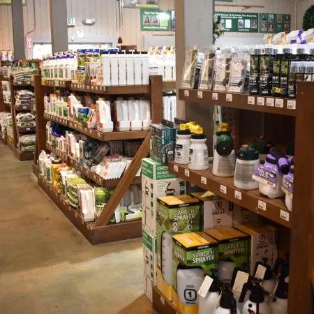 Garden supplies aisle with various sprayers, bottles, and gardening products on wooden shelves in a store.