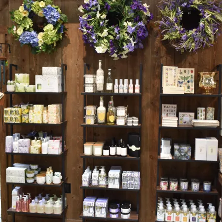 Wooden shelves display assorted skincare products and three floral wreaths hang on rustic wooden wall.