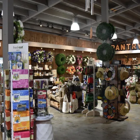 Interior of a rustic gift shop with floral wreaths, greeting cards, hats, and decorative items under wooden beams.