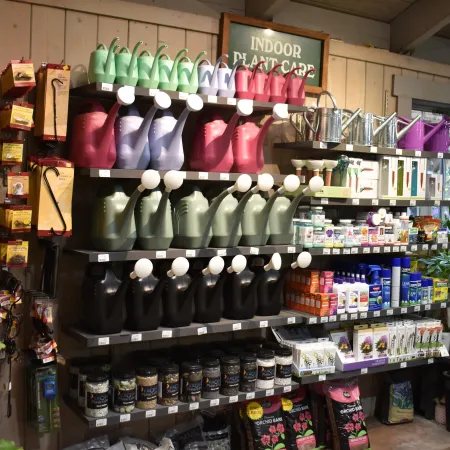 Colorful watering cans and plant care products displayed on shelves in a gardening store section for indoor plants.