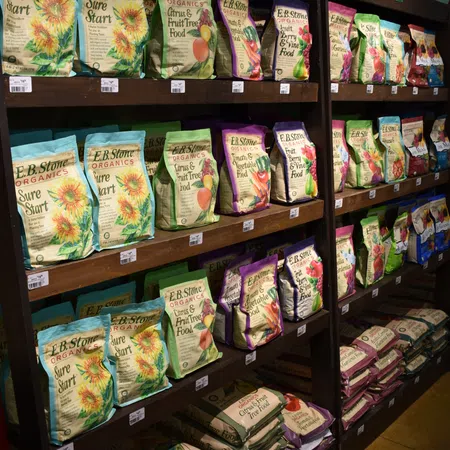 Shelves stocked with colorful E.B. Stone Organics plant food bags and watering cans on top in a garden store.