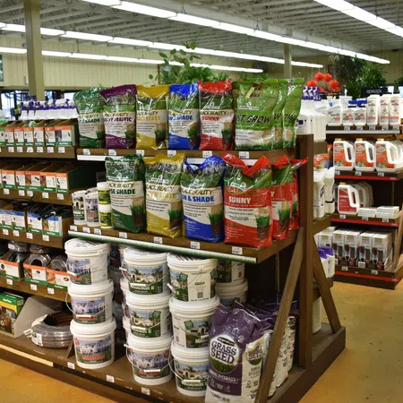 Shelves in a garden store stocked with grass seed bags, fertilizer buckets, and gardening supplies under fluorescent lighting.