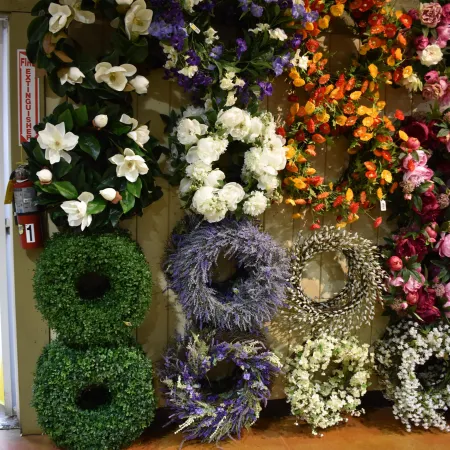 Variety of colorful floral wreaths displayed on a wall with green, white, purple, and orange flowers.