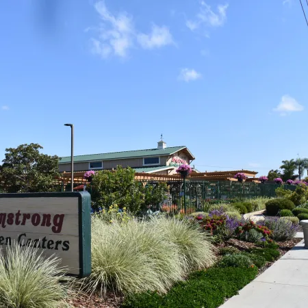 Armstrong Garden Centers sign with lush landscaping and flowers under a clear blue sky beside a sidewalk.