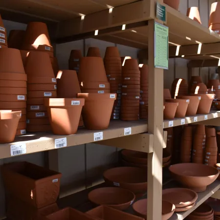 Shelves filled with various sizes and shapes of terracotta plant pots in a garden center under sunlight.