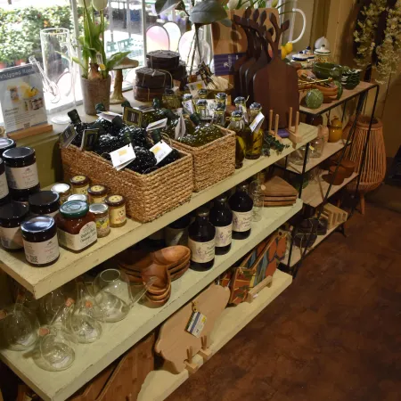 Display of gourmet oils, jams, wooden cutting boards, glassware, and decorative flowers in a cozy store setting