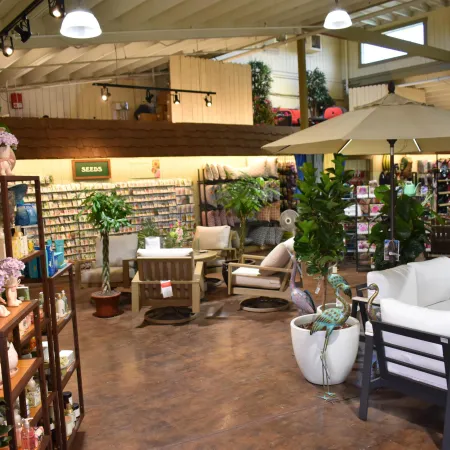 Indoor garden center displaying plants, patio furniture, seeds, and gardening supplies under bright lighting.