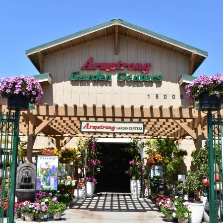 Entrance to Armstrong Garden Centers with hanging flower baskets and potted plants on a sunny day.