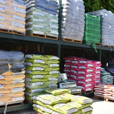 Stacks of colorful potting soil and planting mix bags organized on metal racks outdoors.