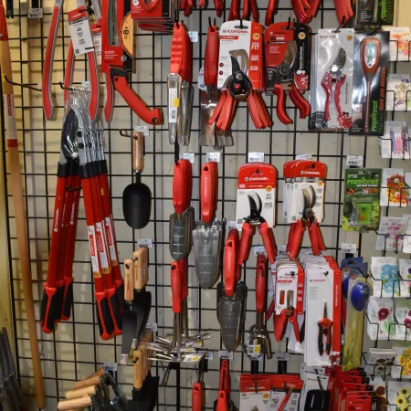 Red-handled gardening tools including pruners, trowels, and loppers displayed on a grid wall in a store.