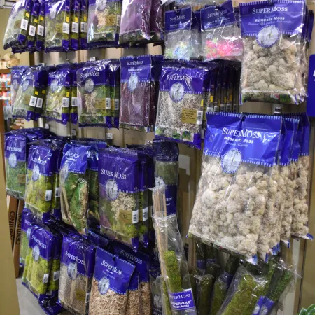 Retail display of various SuperMoss packaged moss products hanging and standing on shelves under bright lighting.