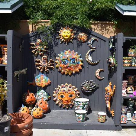 Colorful ceramic sun, moon, octopus, and pumpkin decorations displayed on a garden shelf outdoors