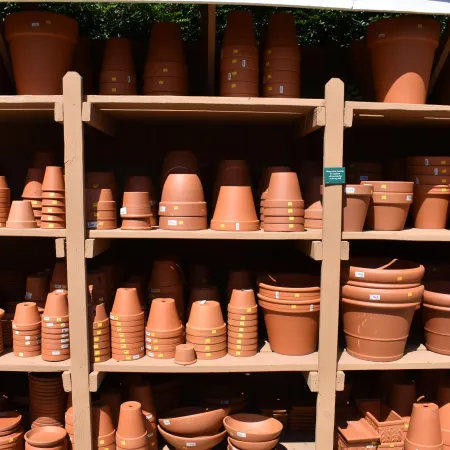 Shelves filled with various sizes of stacked terracotta plant pots in a garden center under sunlight.