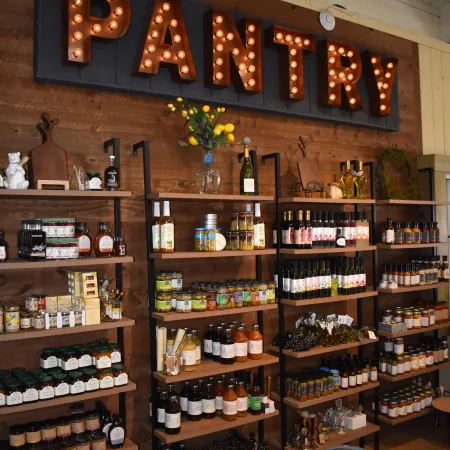 Rustic pantry shelves stocked with jars, bottles, and food items under illuminated marquee pantry sign.